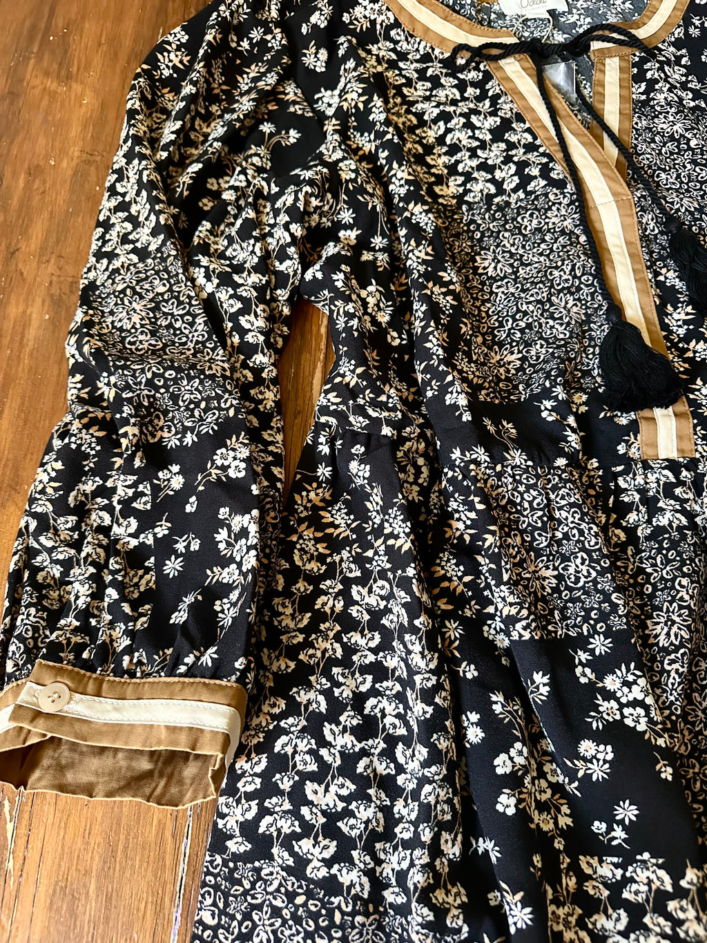 Ditsy Floral Printed Dress with 3/4 sleeves, flowy silhouette, and side pockets in black and beige tones. Features buttoned cuffs and tassel tie neckline.