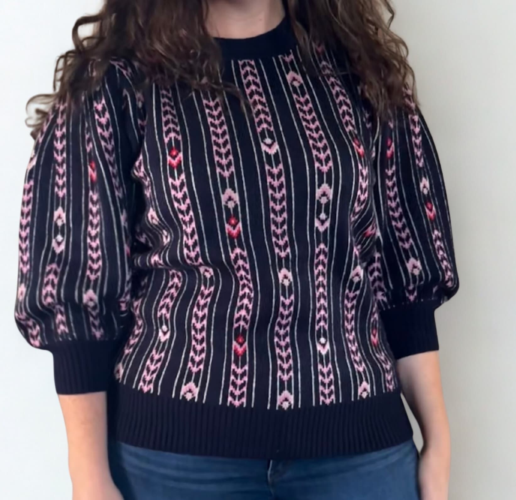 Person wearing a black and pink patterned sweater against a plain background