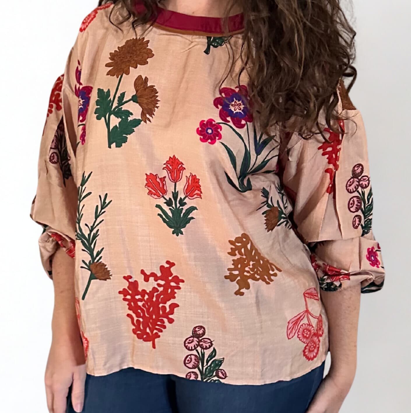 Beige blouse with floral patterns worn by a person on a white background