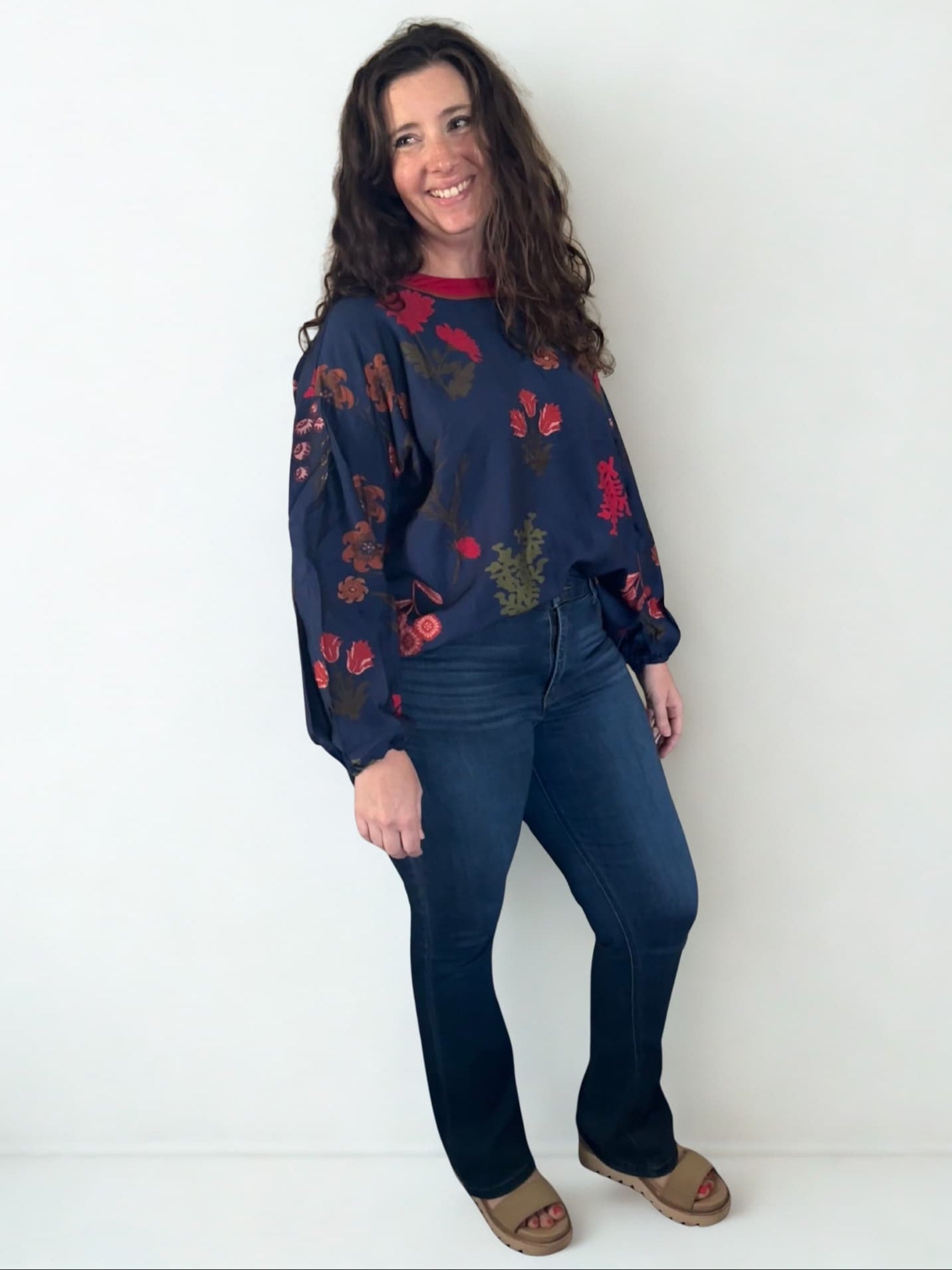 Woman wearing a navy sweater with red floral patterns and blue jeans against a white background