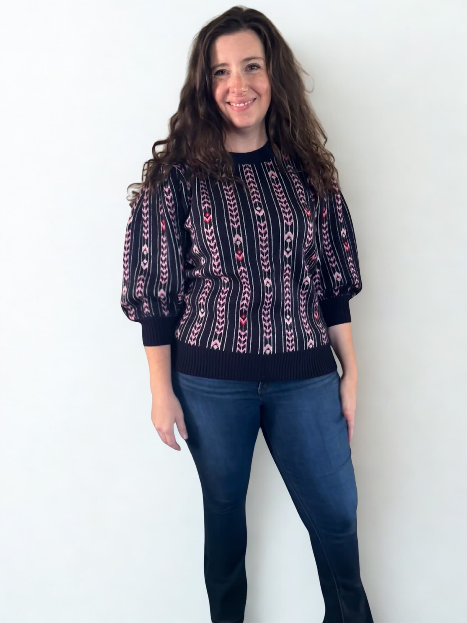 Woman wearing a patterned sweater and jeans against a white background