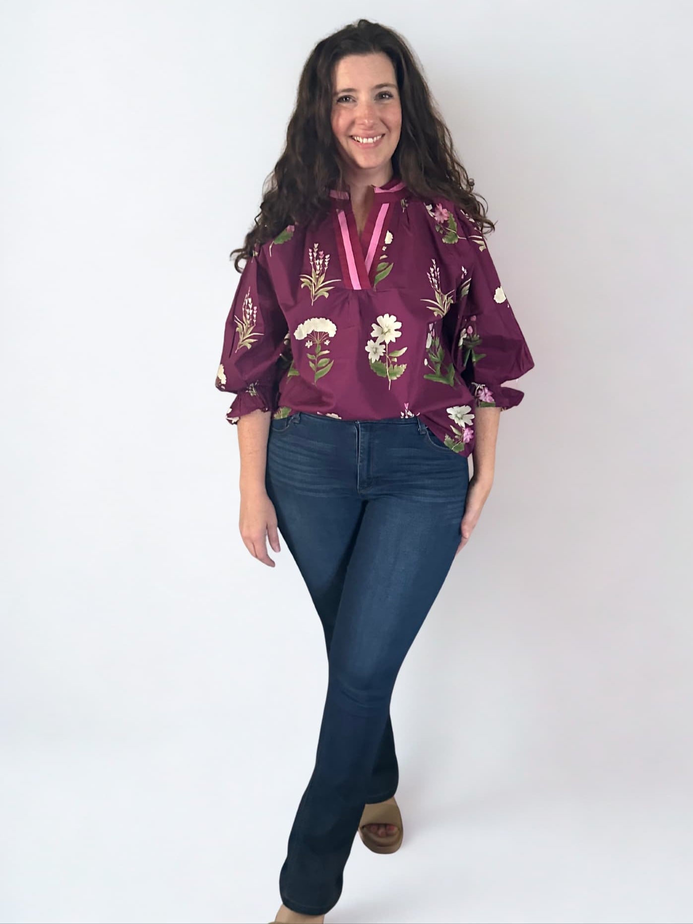 Woman wearing a purple floral blouse and blue jeans against a white background