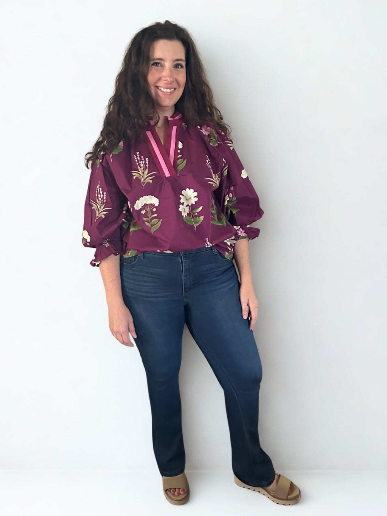 Woman wearing a purple floral blouse and blue jeans against a white background