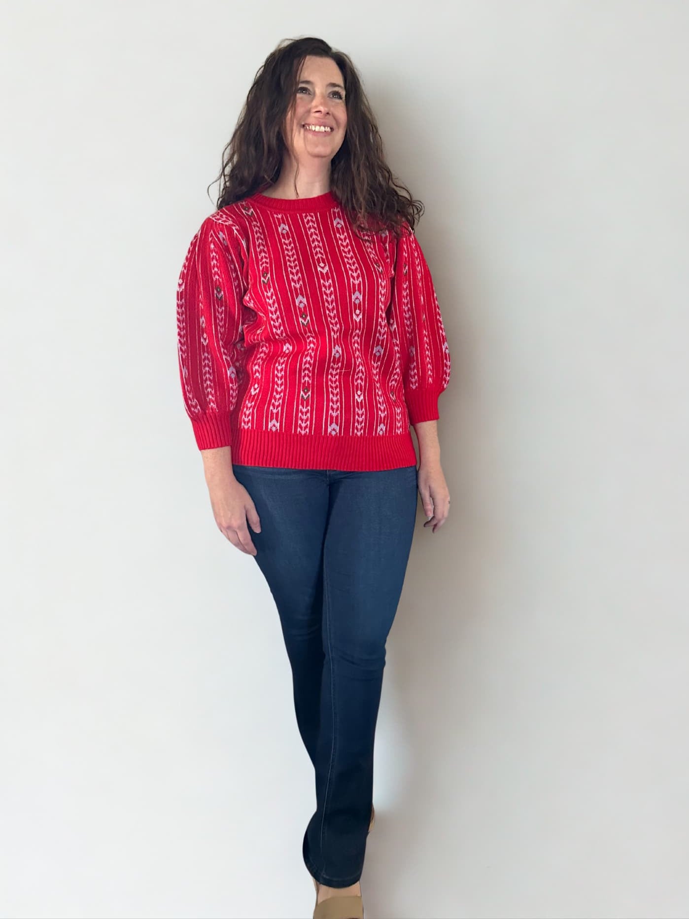 Woman wearing a red patterned sweater and blue jeans against a white background