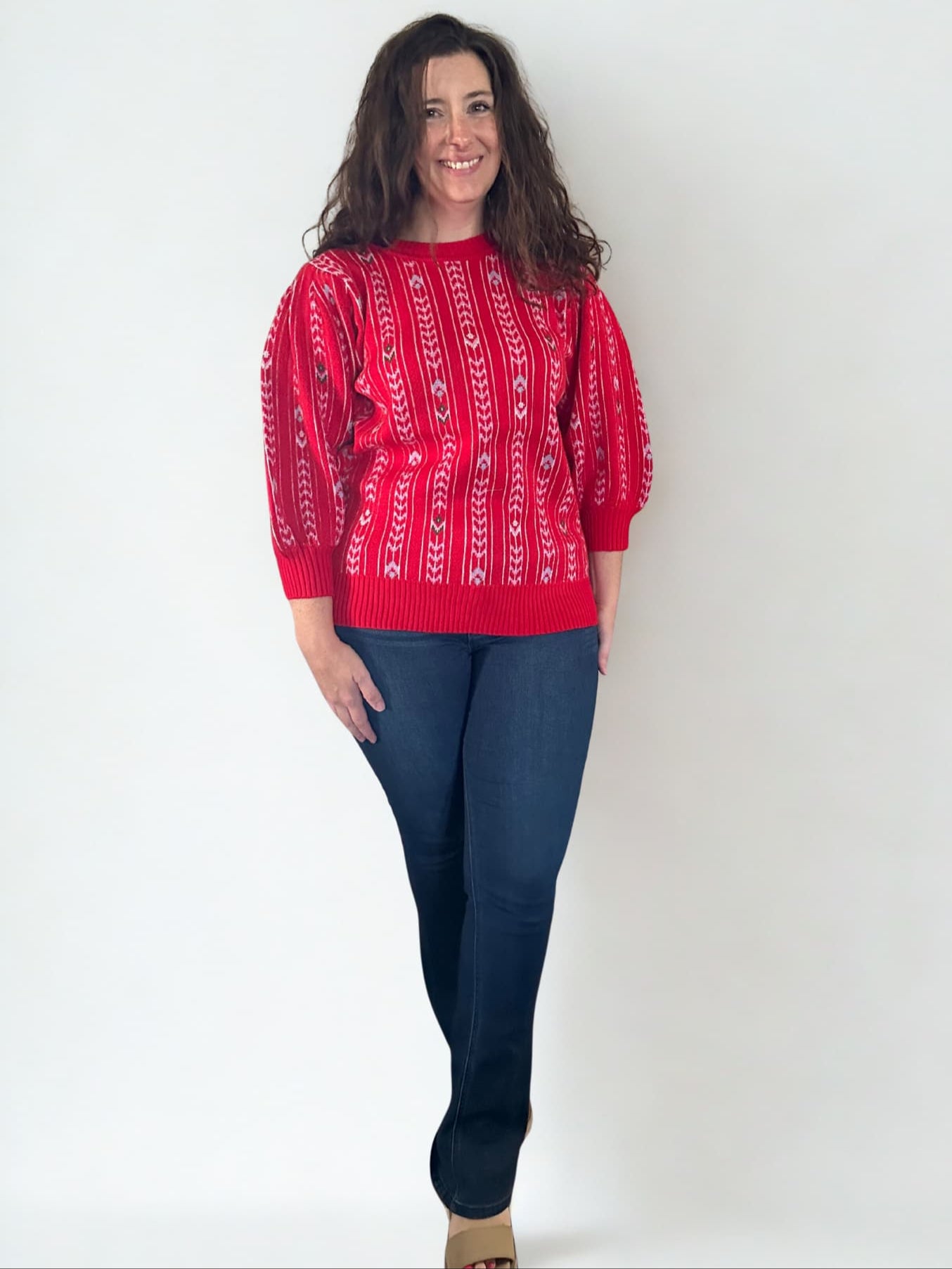 Woman wearing a red patterned sweater and blue jeans against a white background