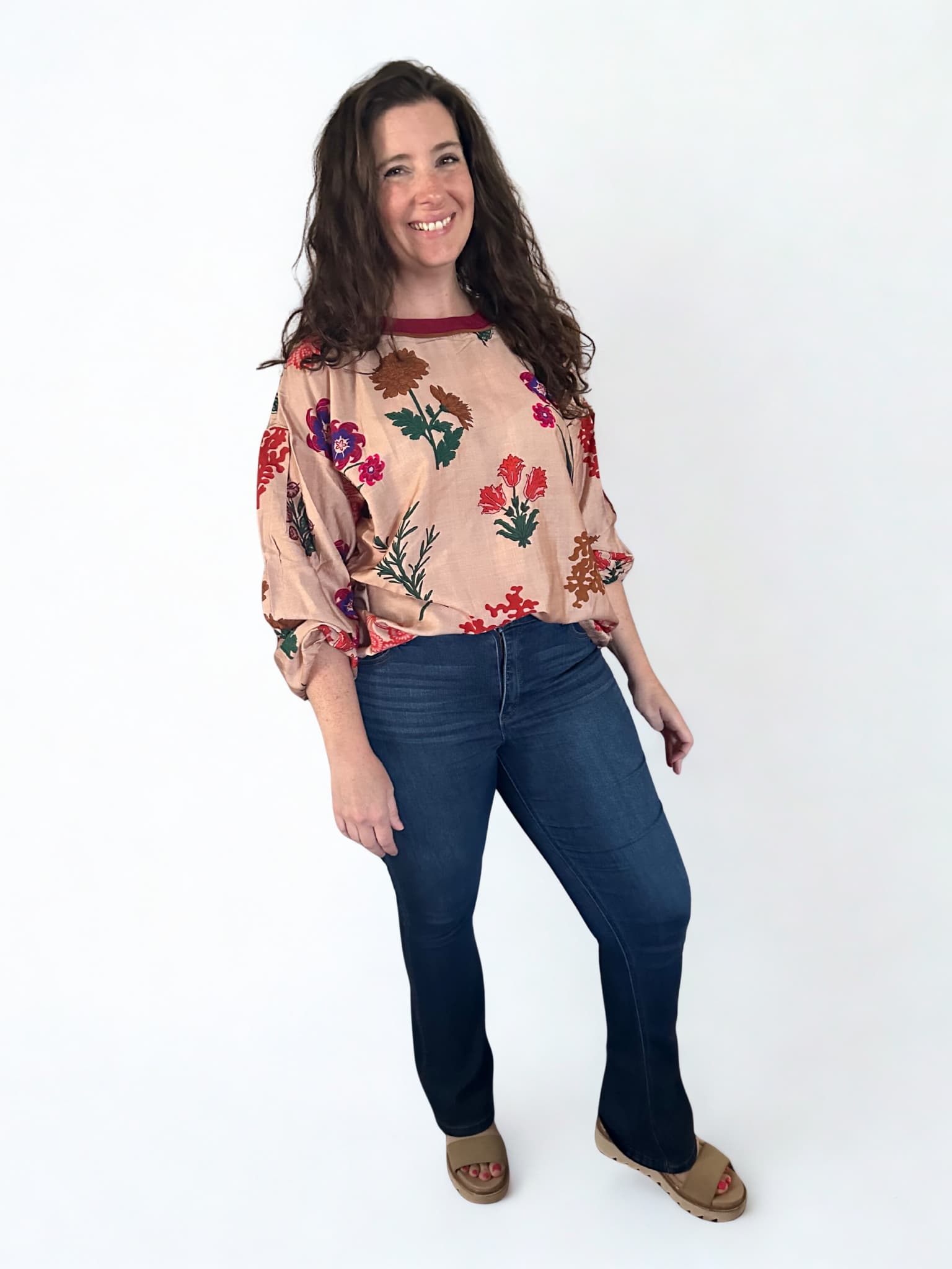 Woman wearing a floral blouse and blue jeans on a white background