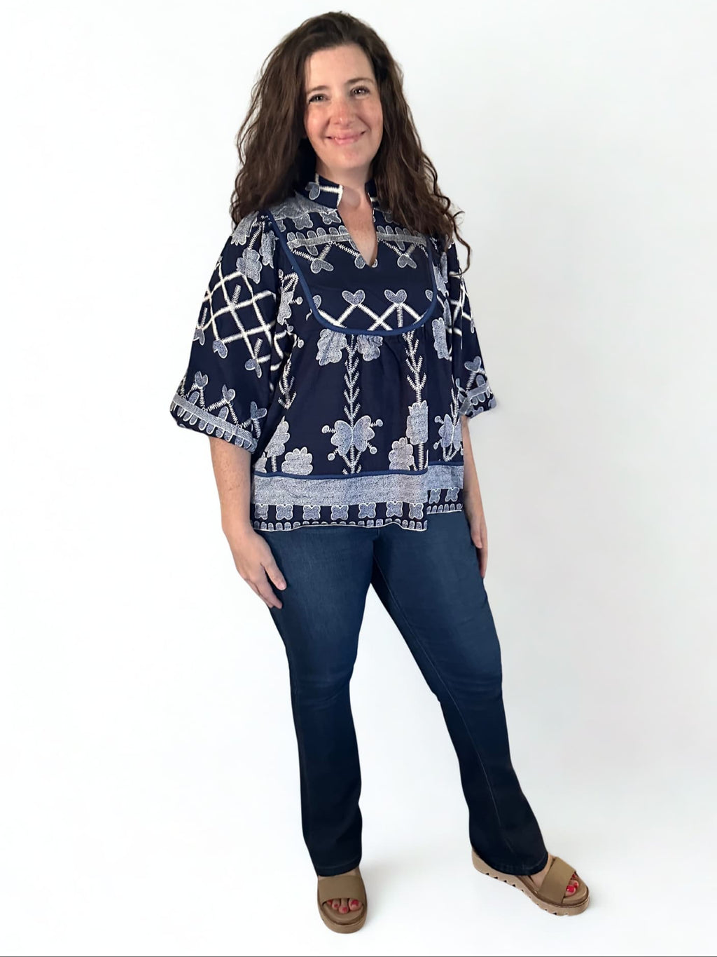 Woman wearing a navy patterned blouse and jeans on a white background