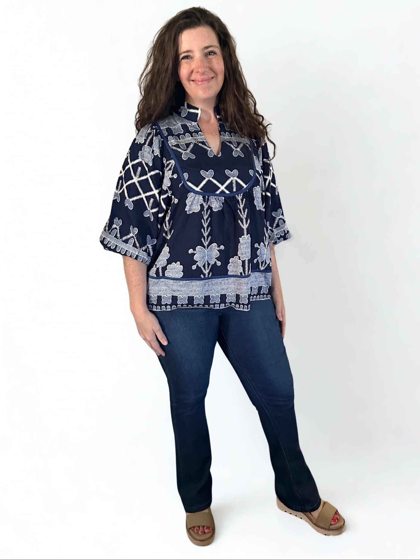 Woman wearing a navy patterned blouse and jeans on a white background