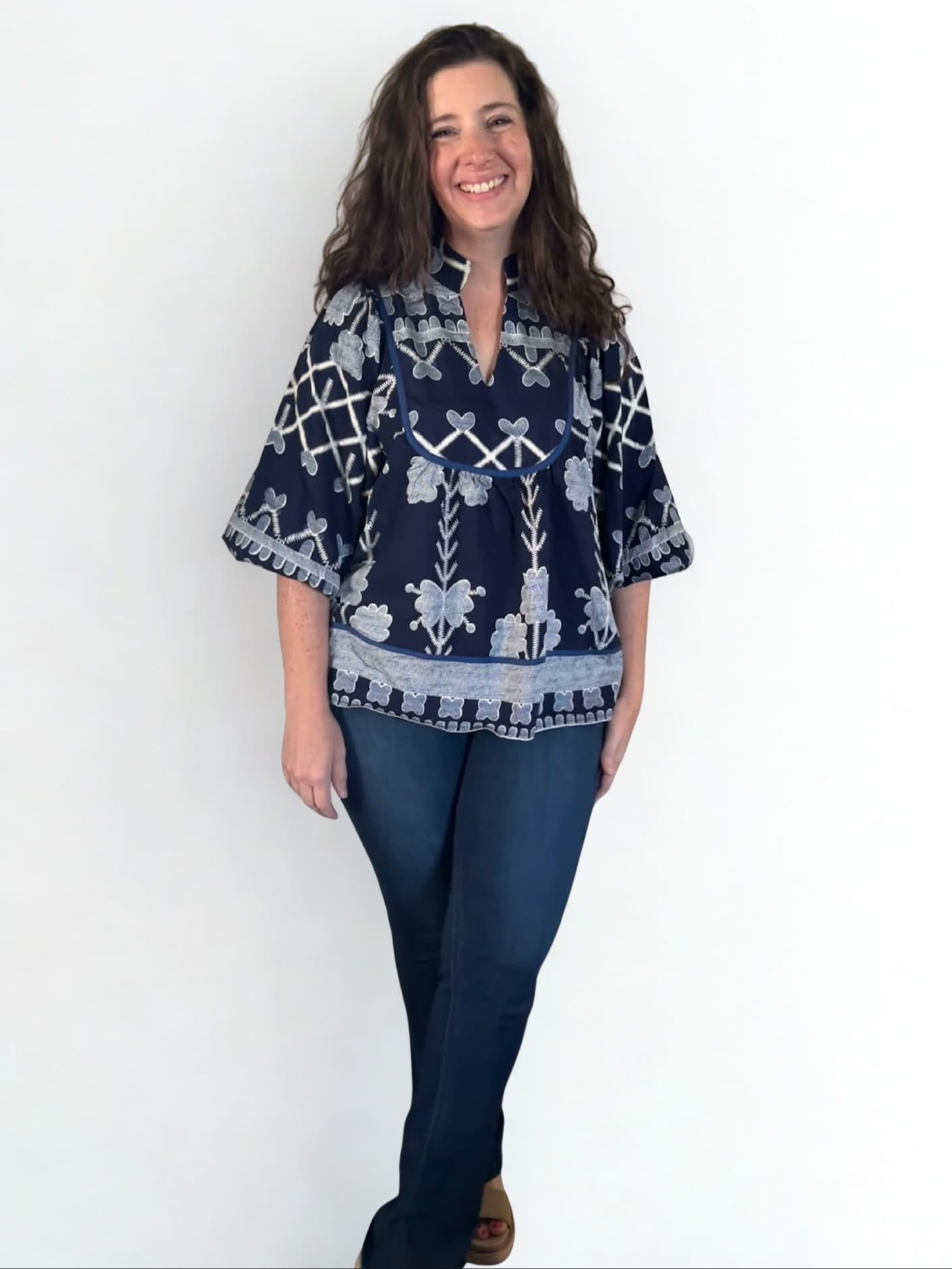 Woman wearing a navy blue patterned top and jeans on a white background