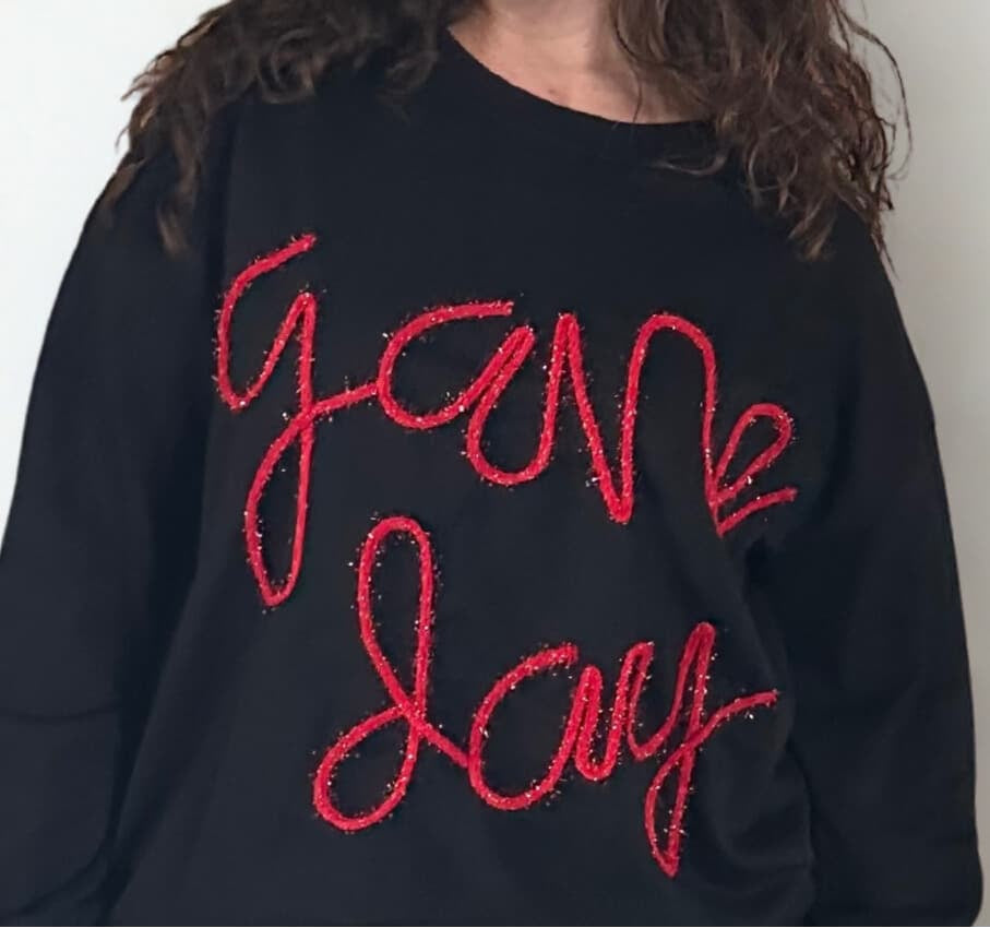 close up of black sweatshirt with game day script in cursive with tinsel
